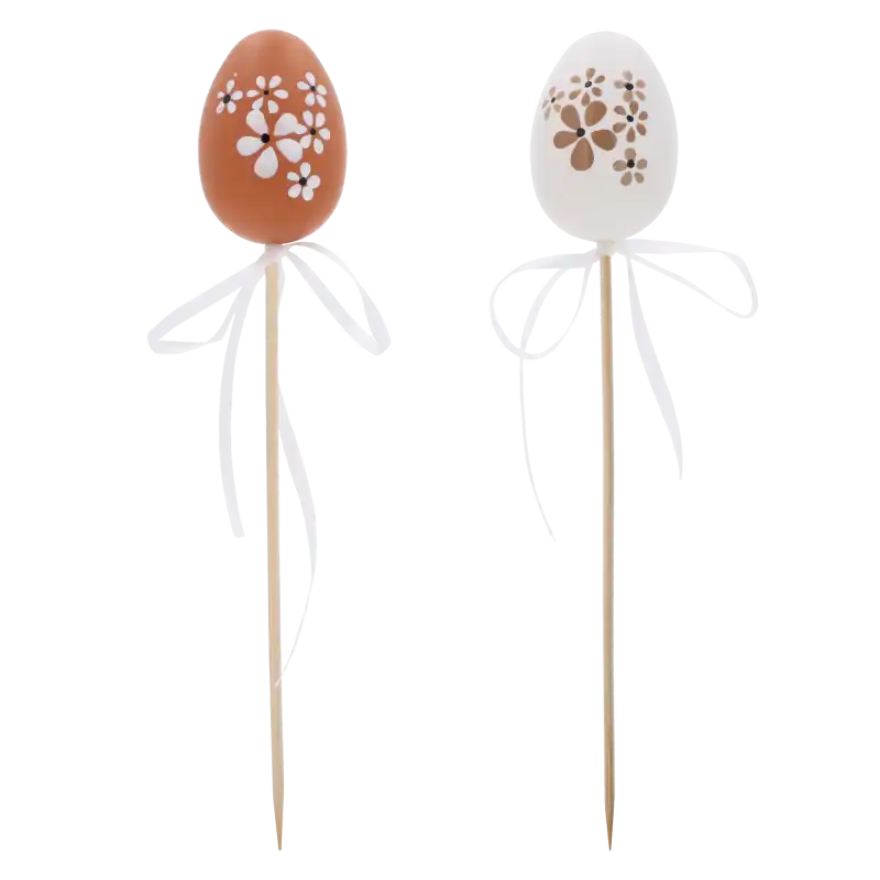Dwie pisanki na piku o wysokości 6 cm, brązowa i biała, ozdobione kwiatowym wzorem z białą kokardką. Dekoracja idealna do wielkanocnych stroików i jaj.