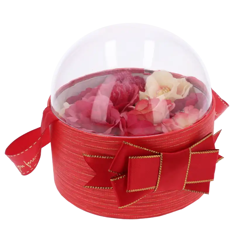 Czerwony flower box 13 cm z przezroczystą pokrywką, wewnątrz którego umieszczono kompozycję z kwiatów w czerwonych odcieniach.
