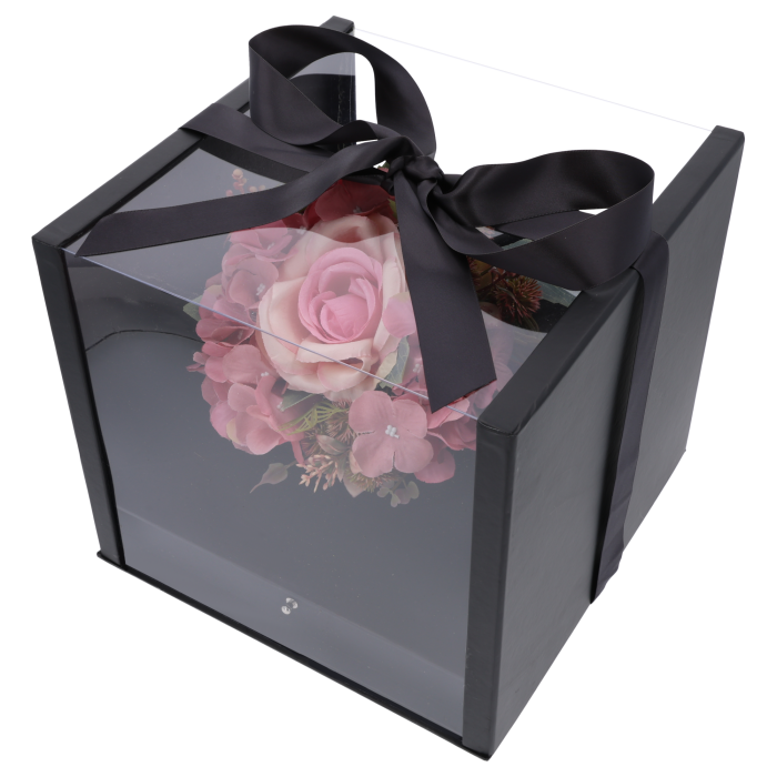 Przezroczysty flower box w kolorze czarnym z ozdobną satynową wstążką zawiązaną w kokardę. Wewnątrz widoczna kompozycja kwiatowa w kształcie serca.