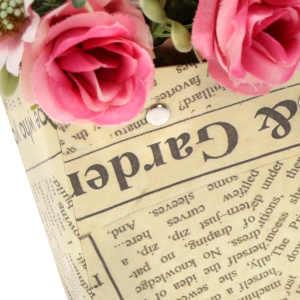 Zbliżenie na strukturę papieru z nadrukiem a'la gazeta oraz metalowe mocowania uchwytów w torebce kwiatowej.