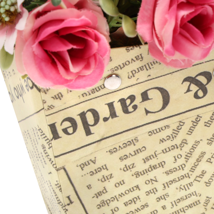 Zbliżenie na strukturę papieru z nadrukiem a'la gazeta oraz metalowe mocowania uchwytów w torebce kwiatowej.