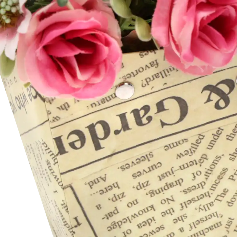 Zbliżenie na strukturę papieru z nadrukiem a'la gazeta oraz metalowe mocowania uchwytów w torebce kwiatowej.