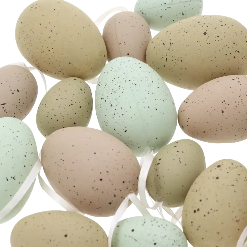 Zbliżenie na mix nakrapianych pisanek w kolorach niebieskim i zielonym, każda posiada przymocowaną wstążeczkę.