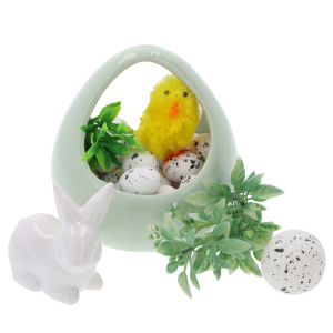 Wielkanocna kompozycja z wykorzystaniem nakrapianych jajeczek, ceramicznego koszyczka, zielonych gałązek oraz figurki białego zajączka na jasnym tle.