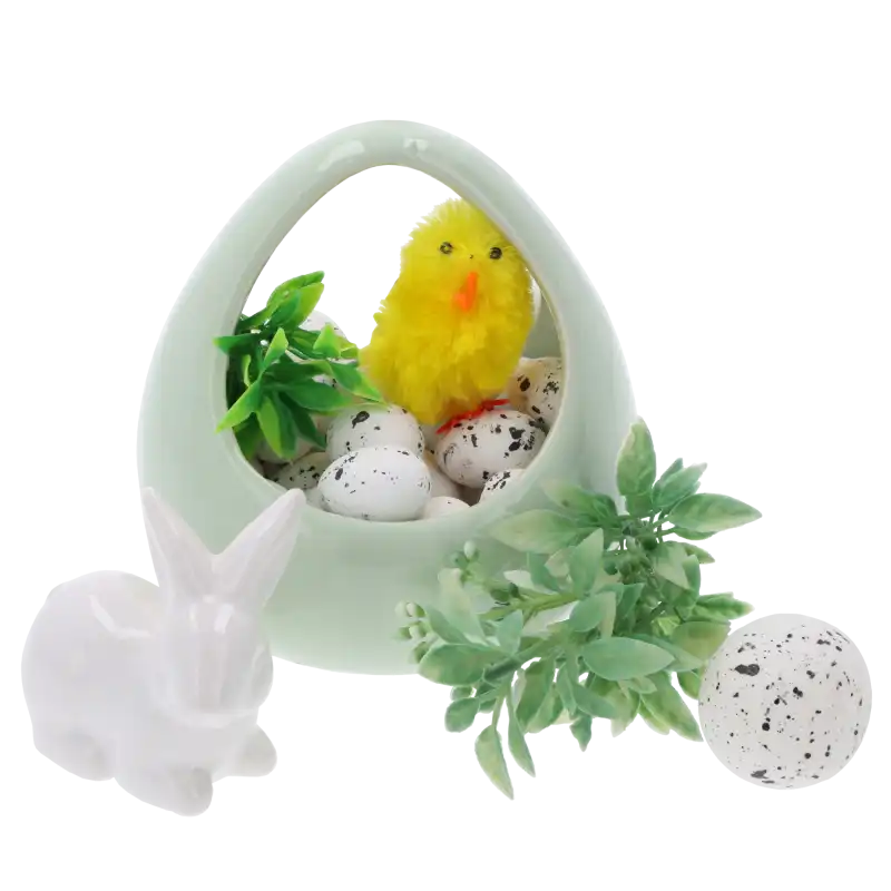 Wielkanocna kompozycja z wykorzystaniem nakrapianych jajeczek, ceramicznego koszyczka, zielonych gałązek oraz figurki białego zajączka na jasnym tle.