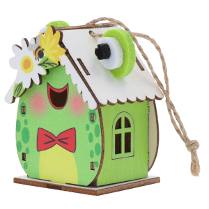 Drewniany domek zawieszka z motywem żaby o wysokości 7 cm, ozdobiony filcowymi oczami i jutowym sznurkiem do zawieszenia.