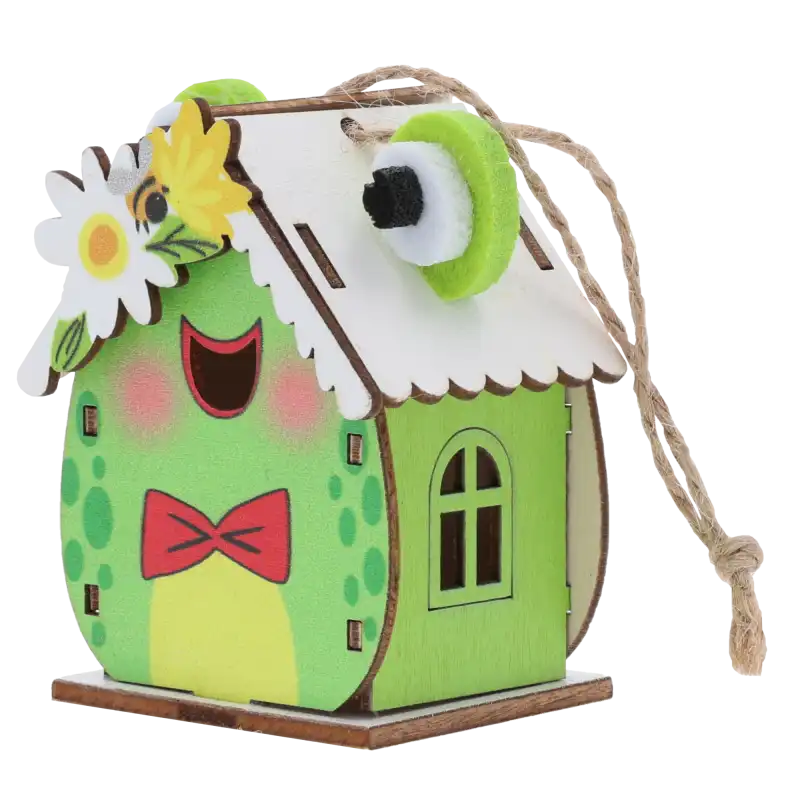 Drewniany domek zawieszka z motywem żaby o wysokości 7 cm, ozdobiony filcowymi oczami i jutowym sznurkiem do zawieszenia.