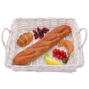 Biały wiklinowy kosz wypełniony sztucznym pieczywem i owocami. Przykład praktycznego zastosowania kosza w kuchni lub jadalni.
