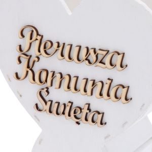 Zbliżenie na precyzyjnie wykonany grawerunek napisu Pierwsza Komunia Święta na białym drewnie.