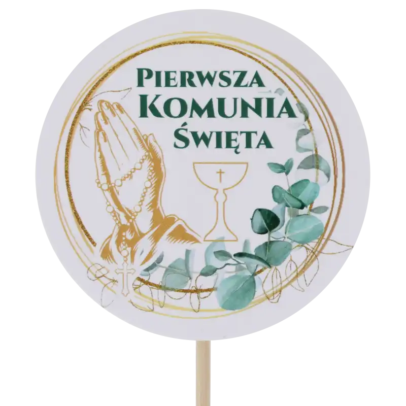 Zbliżenie na okrągły topper komunijny z różańcem i napisem Pierwsza Komunia Święta. Dekoracja o wysokości 29 cm wykonana ze wzmacnianego papieru z ochronną powłoką, umieszczona na drewnianym piku.
