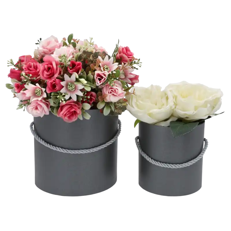 Dwa szare flower boxy wypełnione sztucznymi kwiatami w odcieniach różu i bieli. Dekoracyjna kompozycja w perłowych pudełkach.