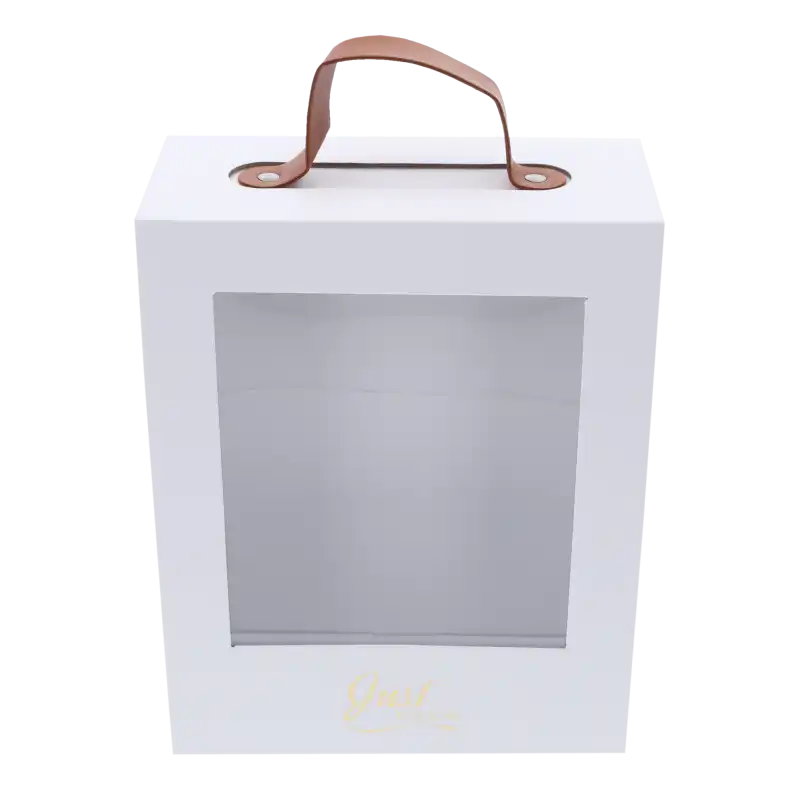 Składany flower box w kolorze białym z zamontowanym uchwytem z imitacji skóry. Pudełko posiada przezroczyste okienko i złoty napis na froncie.