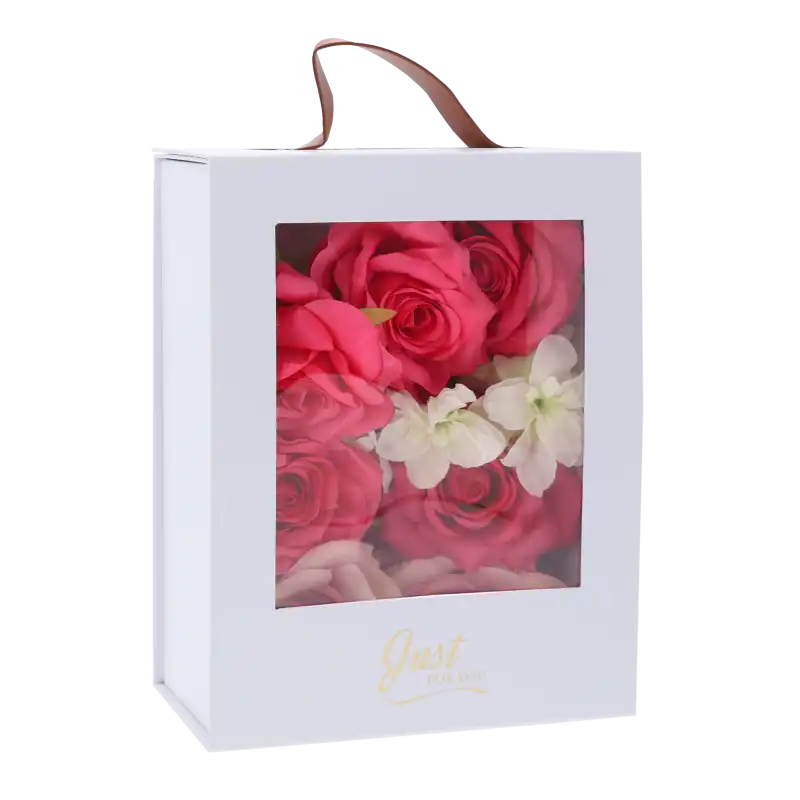Biały składany flower box o wymiarach 23x18x9 cm z przezroczystym okienkiem, uchwytem z imitacji skóry oraz złotym napisem Just For You. Wypełniony kwiatami.