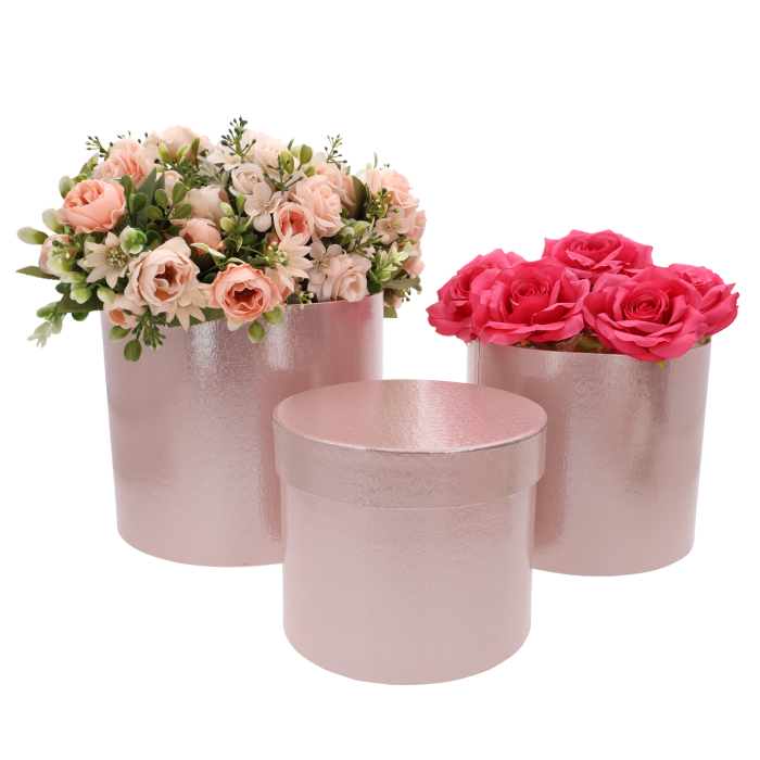 Dwa jasnoróżowe flower boxy wypełnione sztucznymi kwiatami w odcieniach różu, stojące obok pustego pudełka z pokrywką.
