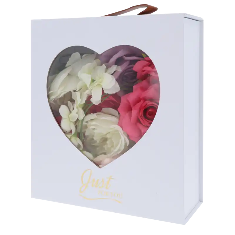 Biały składany flower box 30x25x10 cm z okienkiem w kształcie serca, złotym napisem Just For You i uchwytem, wypełniony kwiatami.