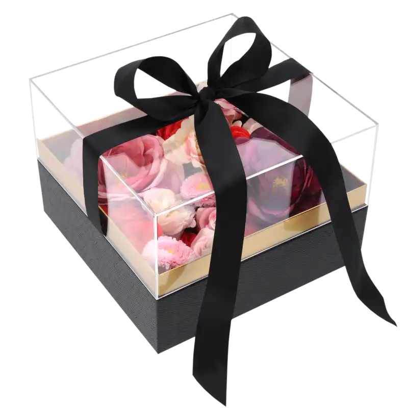Czarny kwadratowy flower box 20x20 cm z przezroczystą pokrywką wypełniony różowymi i czerwonymi kwiatami, przewiązany czarną wstążką.
