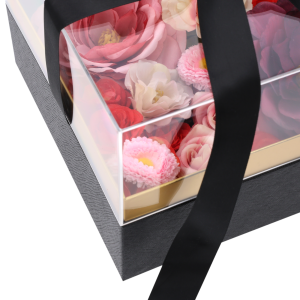 Zbliżenie na wnętrze wypełnionego kwiatami czarnego flower boxa pod przezroczystą pokrywką z przewiązaną czarną wstążką.