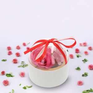 Aranżacja prezentująca flower box o średnicy 13 cm w otoczeniu rozrzuconych płatków kwiatów na jasnym tle.