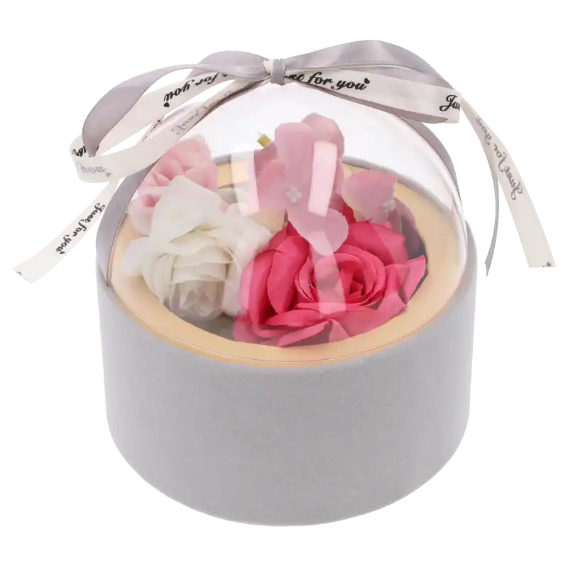 Welurowy flower box w kolorze szarym wypełniony różowymi i białymi kwiatami, zamknięty przezroczystą półkulistą pokrywką.