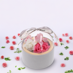 Szary flower box z kwiatami, wyeksponowany na białym tle w otoczeniu rozproszonych płatków róż i zielonych listków.