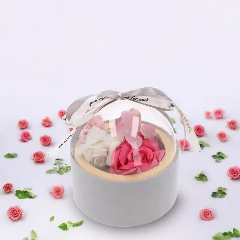 Szary flower box z kwiatami, wyeksponowany na białym tle w otoczeniu rozproszonych płatków róż i zielonych listków.