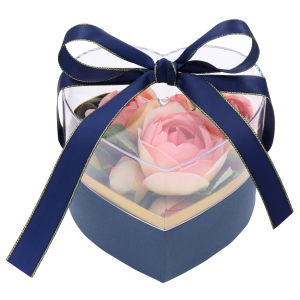 Granatowy flower box wypełniony różowymi sztucznymi kwiatami, zamknięty przezroczystą pokrywką i zawiązany granatową wstążką ze złotym brzegiem.