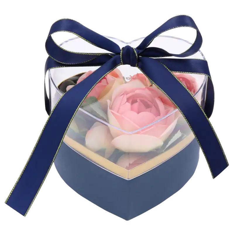 Granatowy flower box wypełniony różowymi sztucznymi kwiatami, zamknięty przezroczystą pokrywką i zawiązany granatową wstążką ze złotym brzegiem.