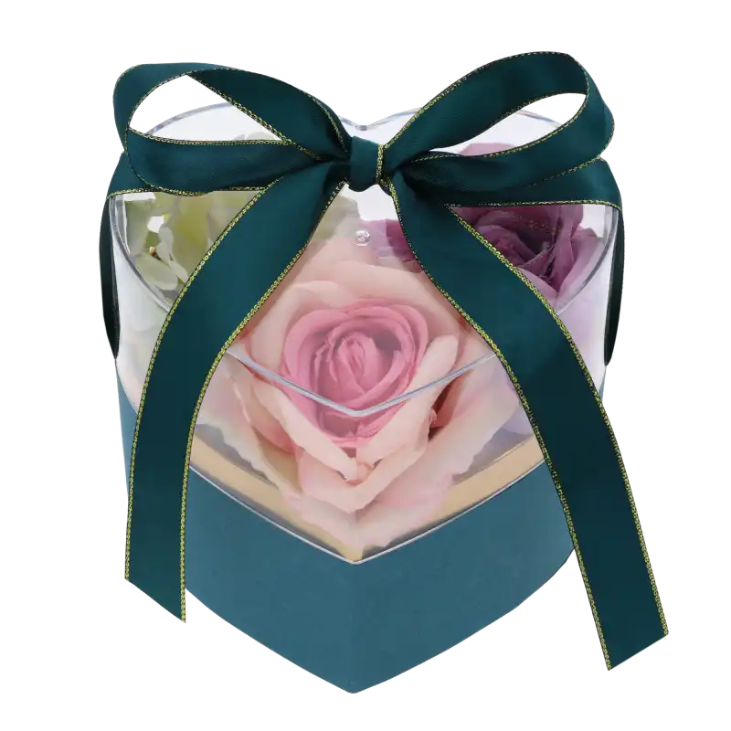 Przezroczysty flower box z wypełnieniem w postaci sztucznych róż w odcieniach różu i bieli. Pudełko zamknięte dekoracyjną kokardą.