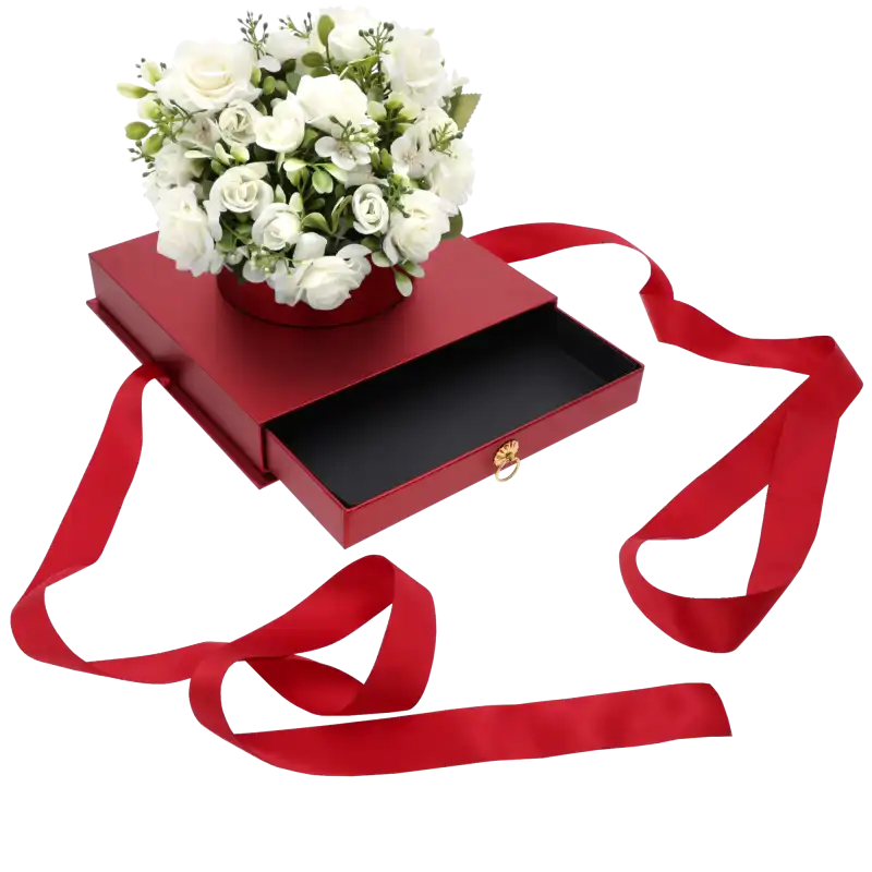 Czerwony flower box z szufladą, na którym umieszczono kompozycję z białych sztucznych róż. Widoczne czerwone wstążki.