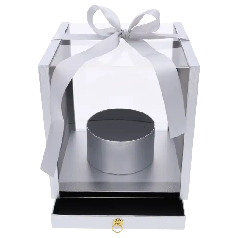 Srebrny flower box o wymiarach 25x25 cm z przezroczystymi ściankami, ozdobną kokardą i wysuwaną szufladą. Pudełko posiada okrągłą osłonkę na kwiaty.