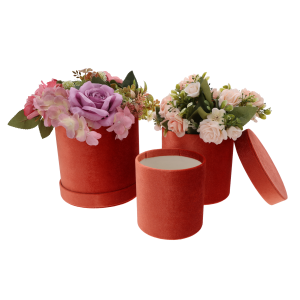 Dwa rudy flower boxy wypełnione sztucznymi kwiatami, obok nich puste pudełko z odłożoną pokrywką na jasnym tle.