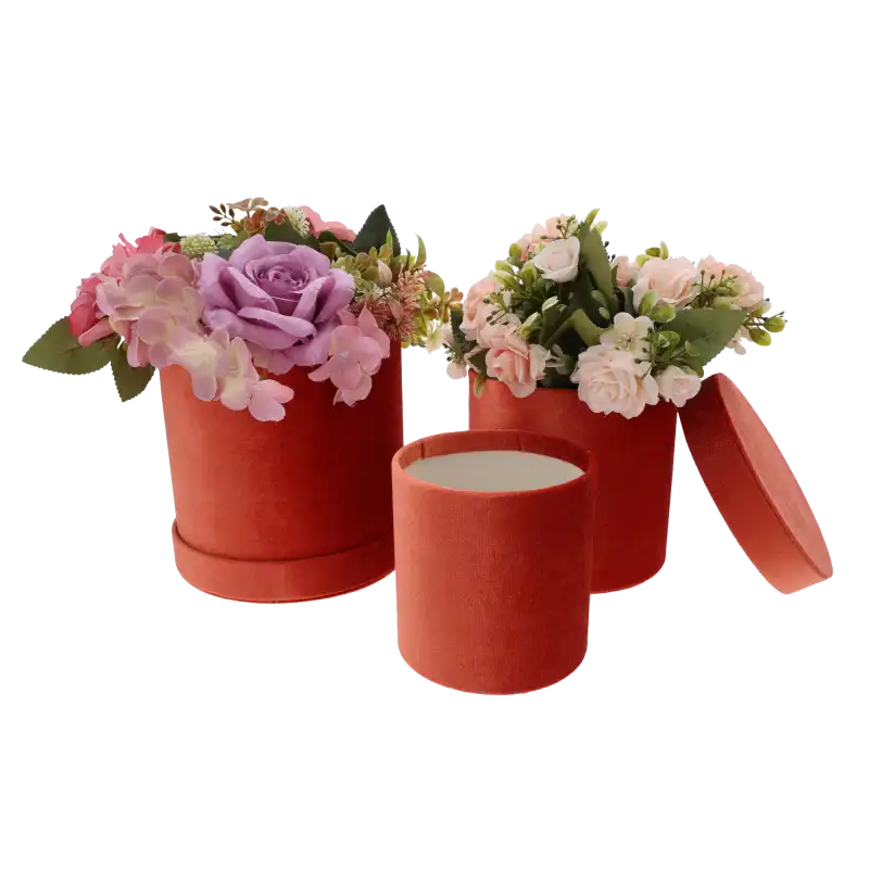 Dwa rudy flower boxy wypełnione sztucznymi kwiatami, obok nich puste pudełko z odłożoną pokrywką na jasnym tle.