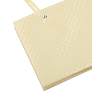 Zbliżenie na detal powierzchni kremowej torebki kwiatowej. Widoczna geometryczna, błyszcząca faktura materiału oraz metalowy nit przy uchwycie.