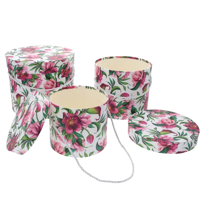 Trzy okrągłe pudełka z nadrukiem roślinnym, z których jedno jest puste i otwarte, a drugie ma położoną obok pokrywkę. W tle trzeci flower box.