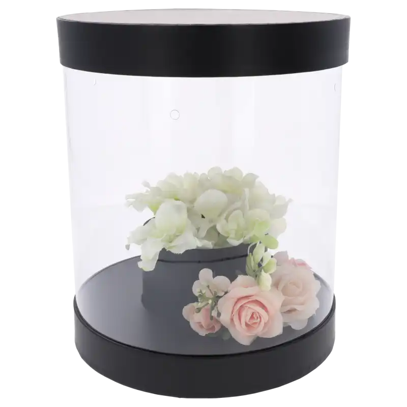 Czarny flower box o średnicy 22 cm z przezroczystymi ściankami. Wewnątrz widoczna kompozycja kwiatowa z różami. Eleganckie opakowanie prezentowe.