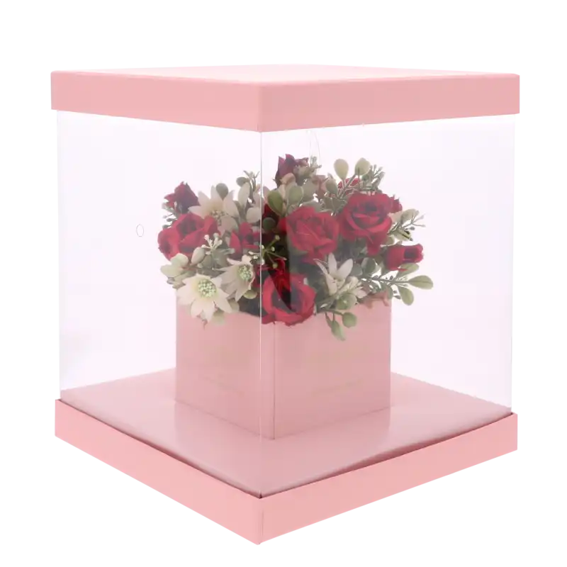 Gotowa kompozycja kwiatowa w różowym pudełku 25x25 cm z przezroczystą osłoną, która eksponuje zawartość pudełka.