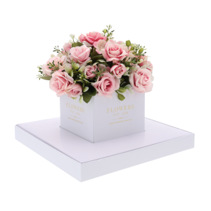 Biały kwadratowy flower box z gotową kompozycją kwiatową w środku. Przezroczyste boki eksponują rośliny, zapewniając im estetyczną oprawę na uroczystość komunijną.