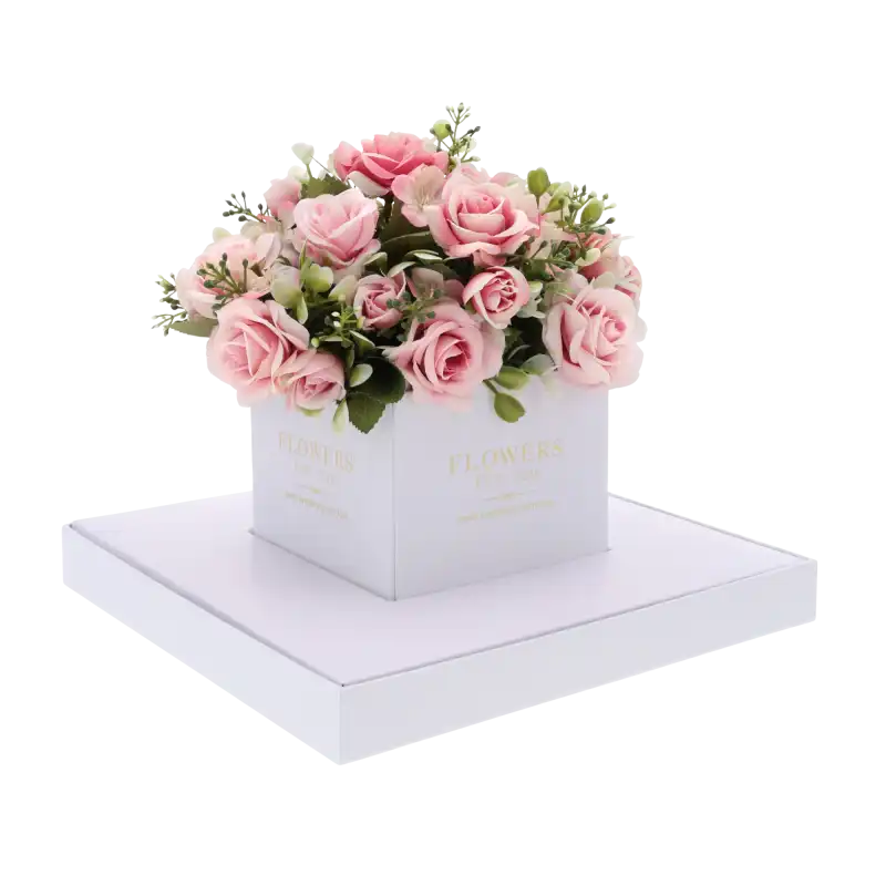 Biały kwadratowy flower box z gotową kompozycją kwiatową w środku. Przezroczyste boki eksponują rośliny, zapewniając im estetyczną oprawę na uroczystość komunijną.