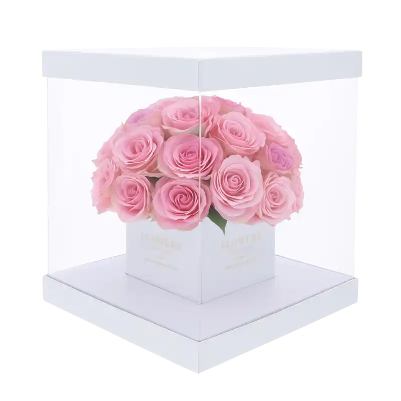 Biały kwadratowy flower box 25x25 cm z przezroczystymi ściankami, wypełniony kompozycją róż. Eleganckie opakowanie na prezent, idealne na pamiątkę pierwszej komunii świętej.