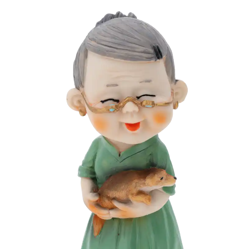 Zbliżenie na figurkę babci z psem, ukazujące detale twarzy, okulary oraz sposób trzymania zwierzątka. Wysokość całkowita wynosi 15 cm.