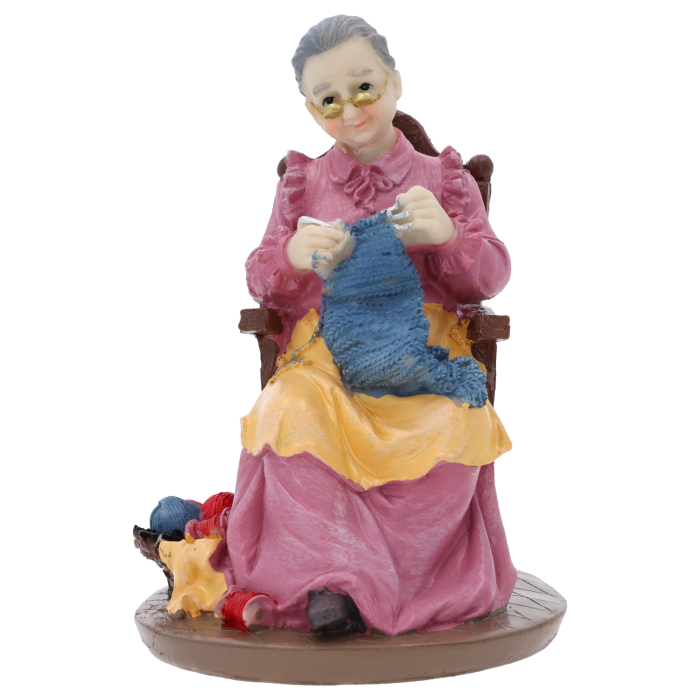 Figurka babcia robiąca na drutach o wysokości 17 cm, wykonana z tworzywa, przedstawia postać w fotelu z robótką ręczną. Idealna dekoracja na Dzień Babci i Dziadka.