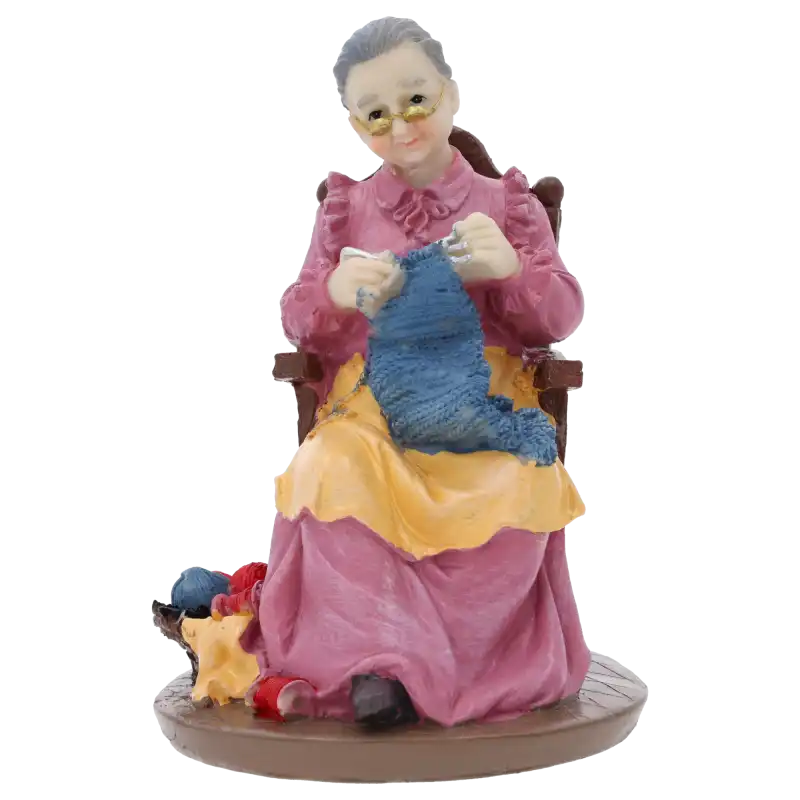 Figurka babcia robiąca na drutach o wysokości 17 cm, wykonana z tworzywa, przedstawia postać w fotelu z robótką ręczną. Idealna dekoracja na Dzień Babci i Dziadka.