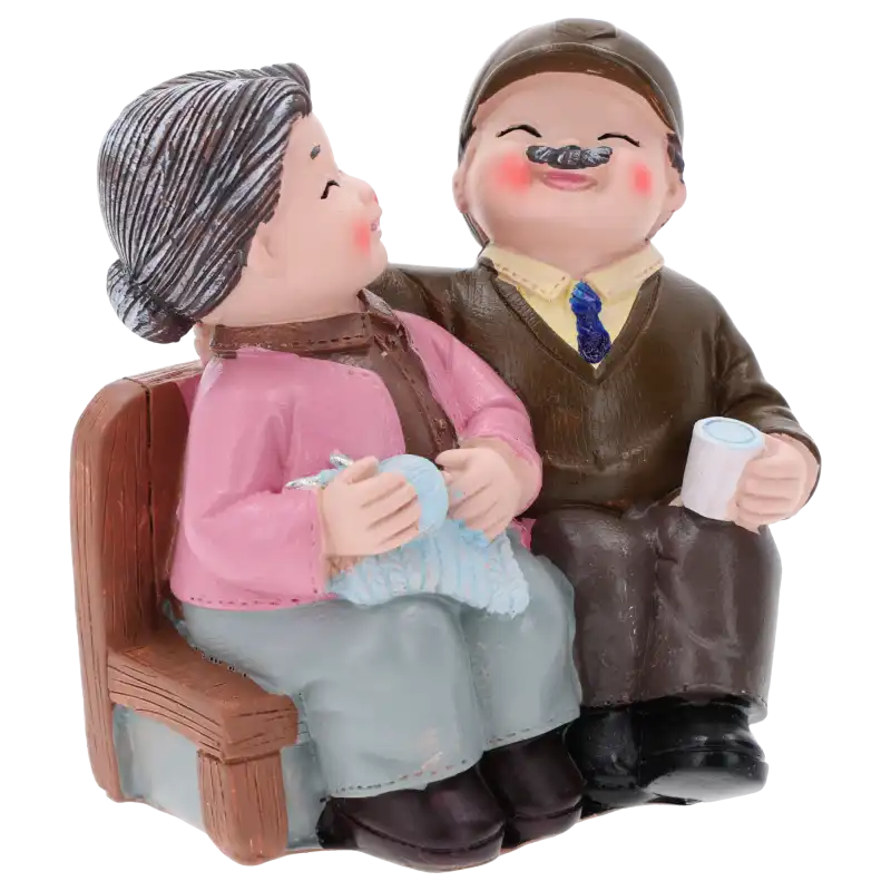 Figurka przedstawiająca babcię i dziadka na ławeczce, ujęcie pod kątem eksponujące detale stroju, w tym sweterki i nakrycie głowy postaci z tworzywa.