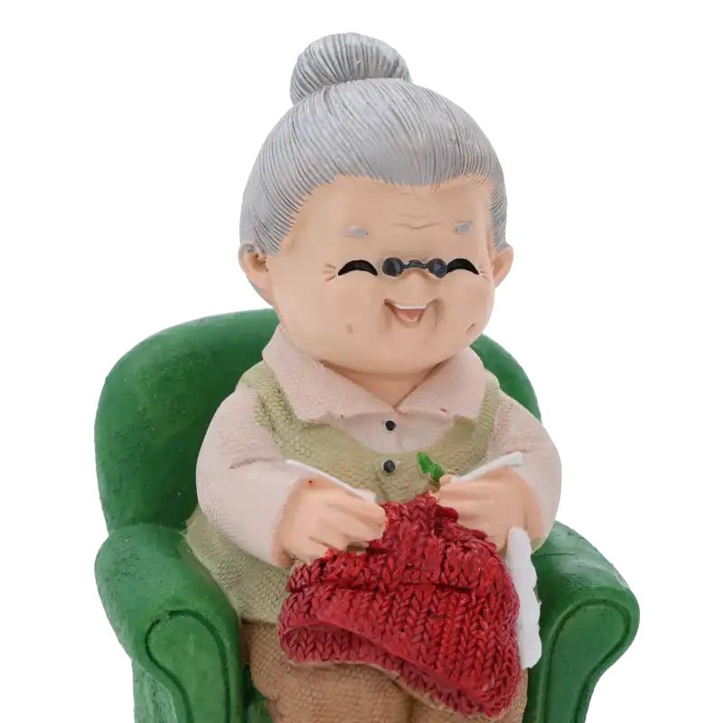 Zbliżenie na twarz i ręce babci robiącej na drutach. Widoczne drobne detale, takie jak okulary i czerwona dzianina, nadające figurce rodzinnego charakteru.
