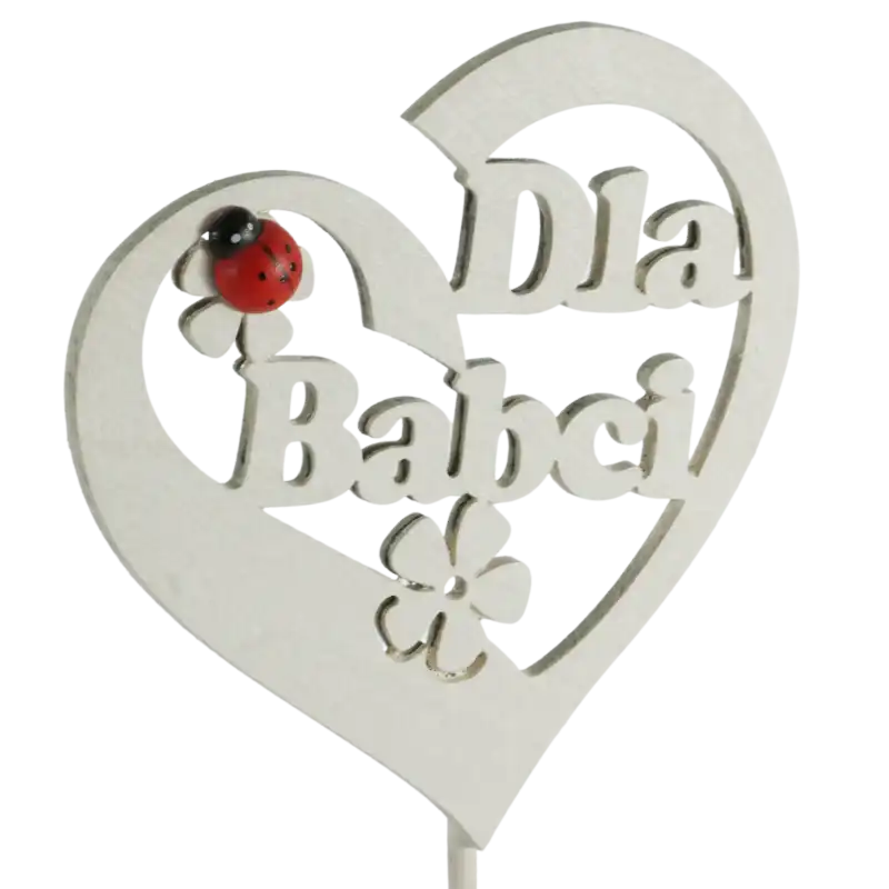 Zbliżenie na ażurowe serce z napisem Dla Babci umieszczone na drewnianym patyczku. Dekoracyjny akcent w postaci czerwonej biedronki wyróżnia się na tle jasnego drewna.