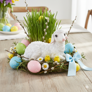 Figurka owieczki w wielkanocnej aranżacji z pisankami, zieloną trawą i baziami, podkreślająca wiosenny charakter ozdoby.