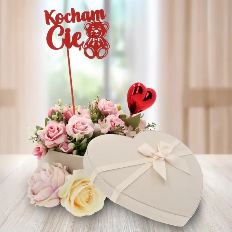 Topper z napisem Kocham Cię umieszczony w dekoracyjnym flowerboxie z kwiatami. Czerwony akcent doskonale komponuje się z romantycznym charakterem kompozycji.