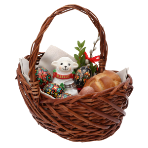 Wiklinowy kosz wypełniony wielkanocnymi dekoracjami, w tym figurką baranka, pisankami, gałązkami i pieczywem na jasnej serwecie.
