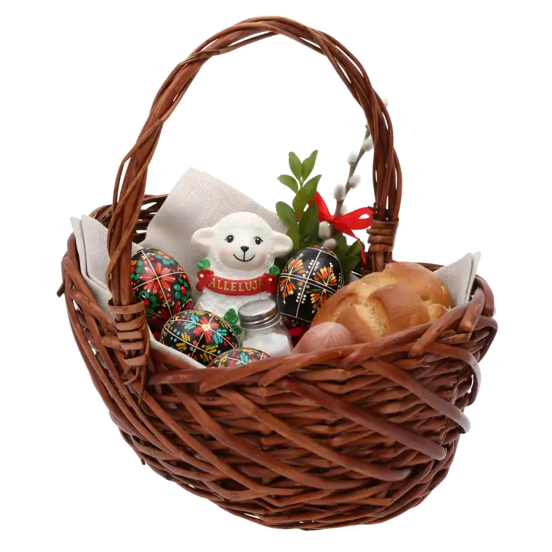 Wiklinowy kosz wypełniony wielkanocnymi dekoracjami, w tym figurką baranka, pisankami, gałązkami i pieczywem na jasnej serwecie.