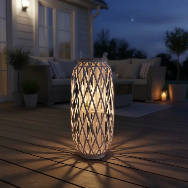 Podświetlony wiklinowy lampion ustawiony na drewnianym tarasie wieczorową porą, tworzący nastrojowy klimat w ogrodowej aranżacji.
